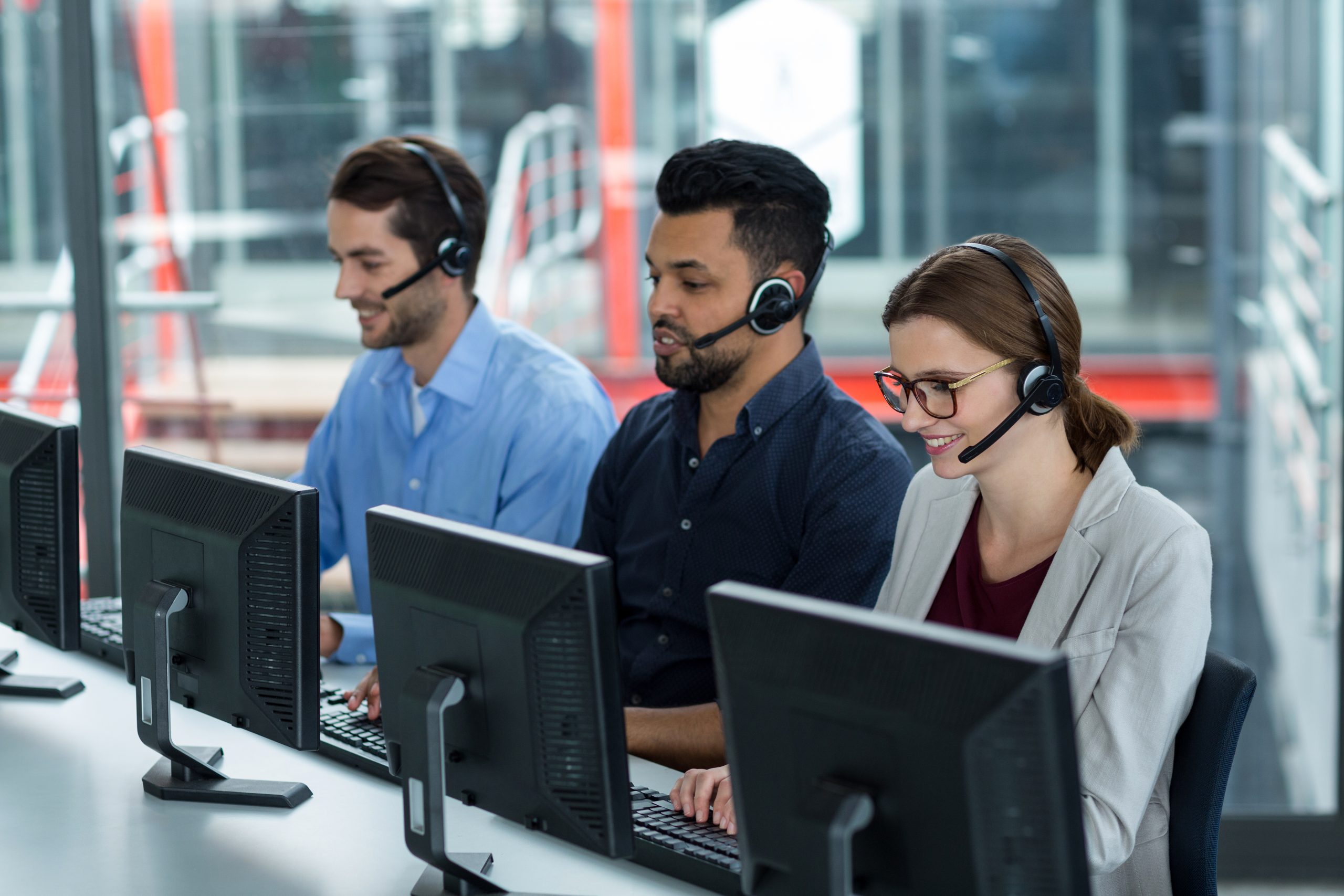 Smiling business executives with headsets using computers at desk in office